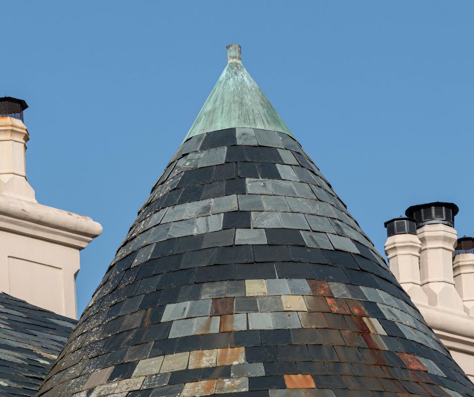 A conical slate turret roof topped with a copper finial on a heritage building